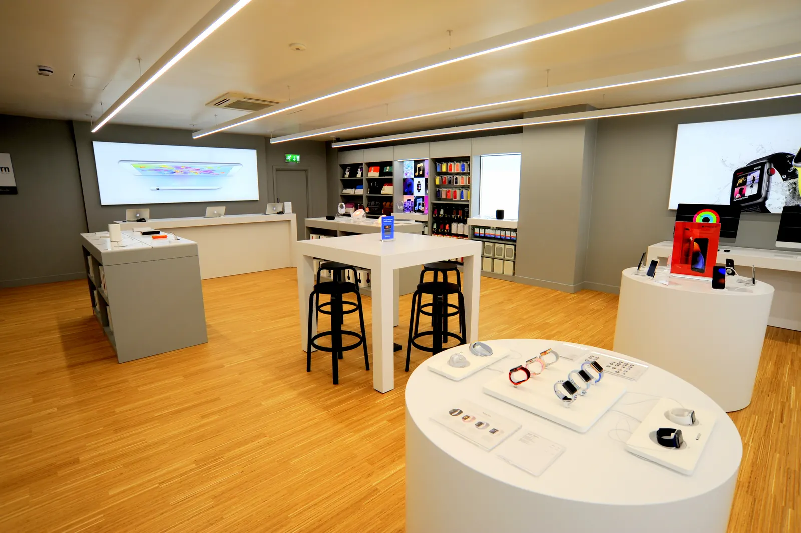 A finished store with high stools, white display tables and a backlit wall graphic